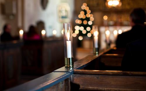 Tända ljus i glasrör står på varje bänkrad i en kyrka.