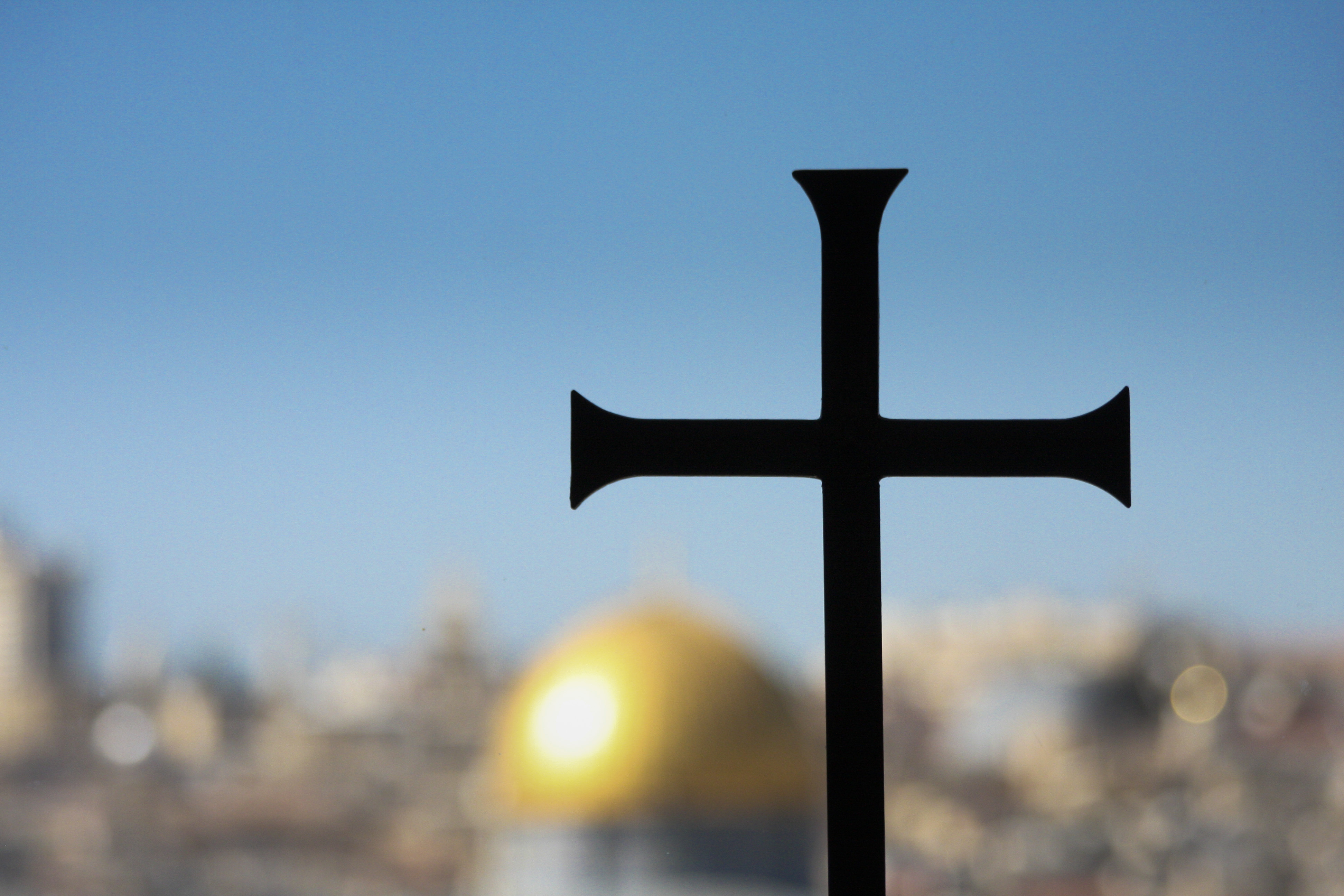 Ett svart kors mot blå himmel. I bakgrunden syns en stad med en gyllene kupol.