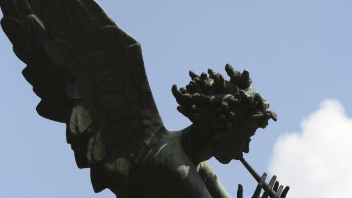 En staty av en ängel som spelar trumpet mot blå och molnig himmel.