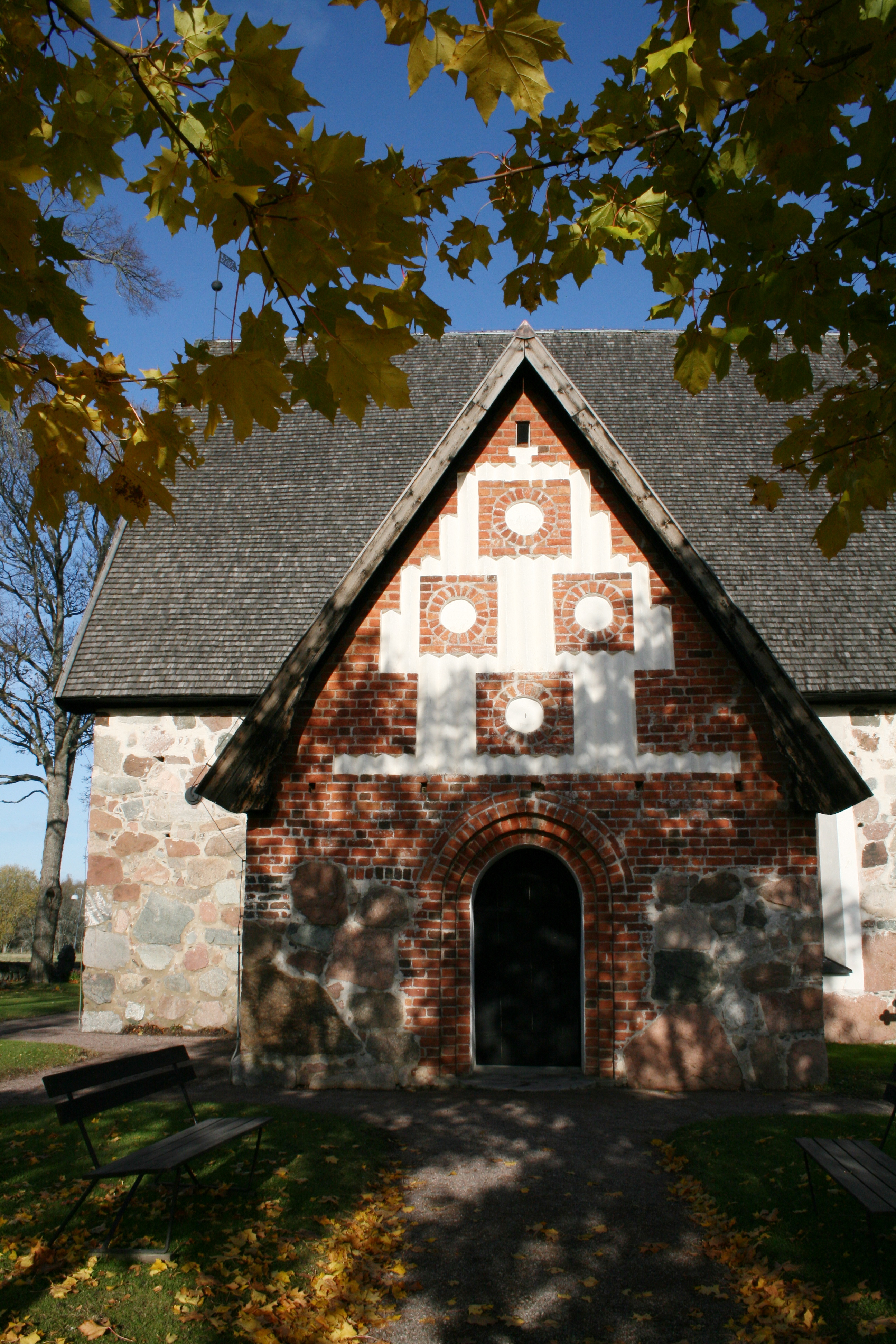 En stenkyrka. Några grenar med höstlöv i förgrunden.