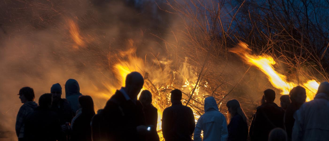 En grupp människor står vid en majbrasa i mörkret.