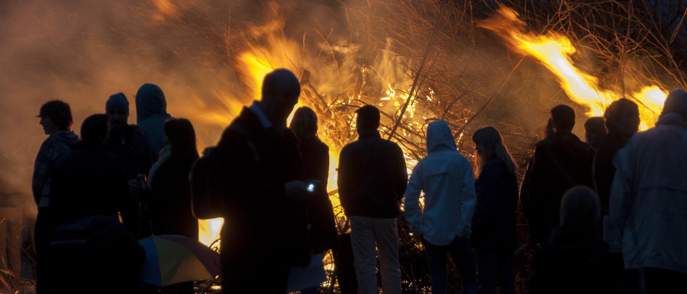 En grupp människor står vid en majbrasa i mörkret.