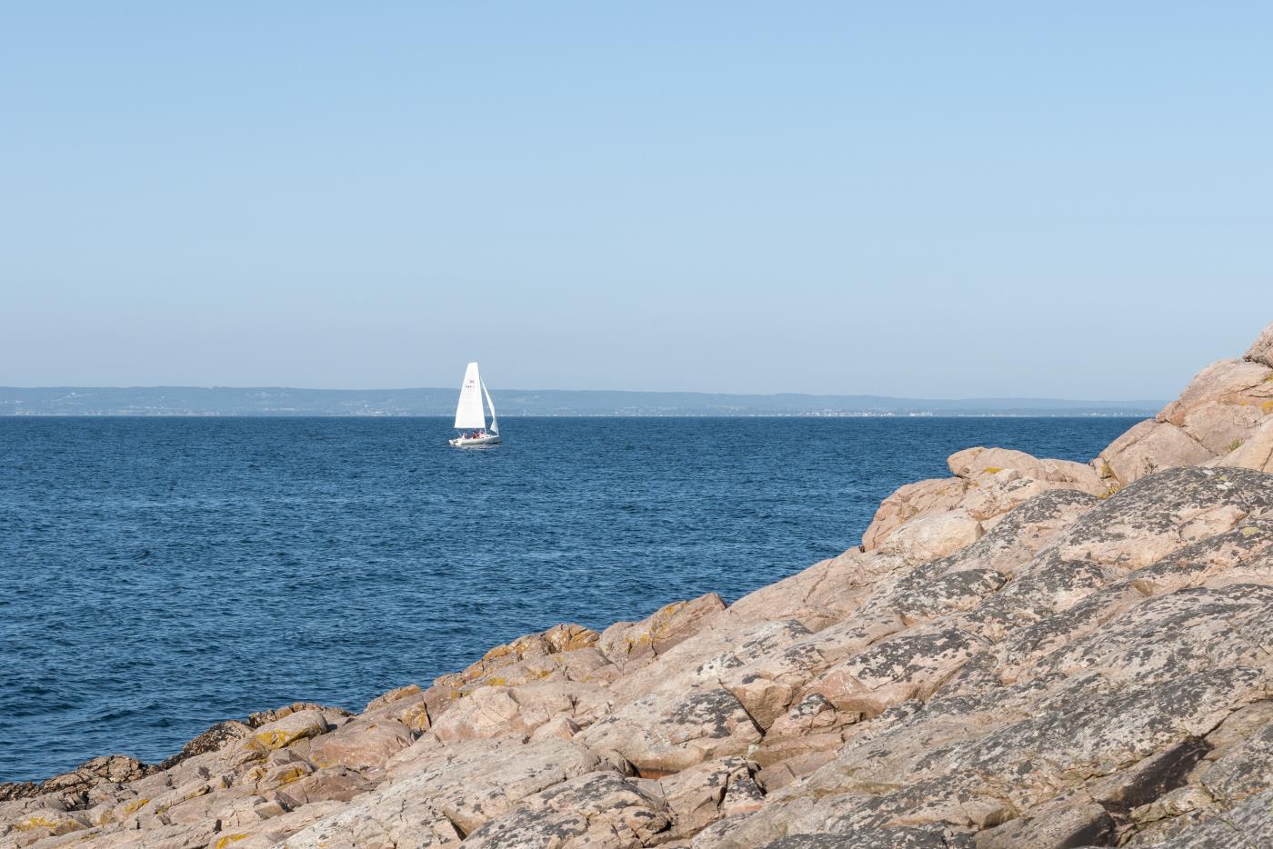 En segelbåt ute på vattnet. Klippor i förgrunden.