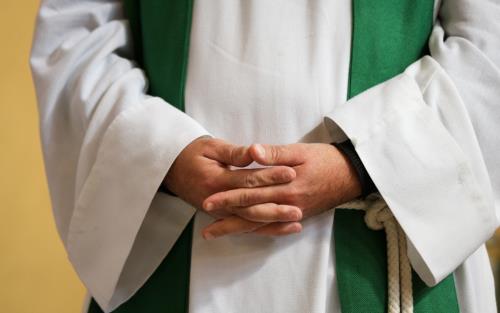 En präst står med knäppta händer.