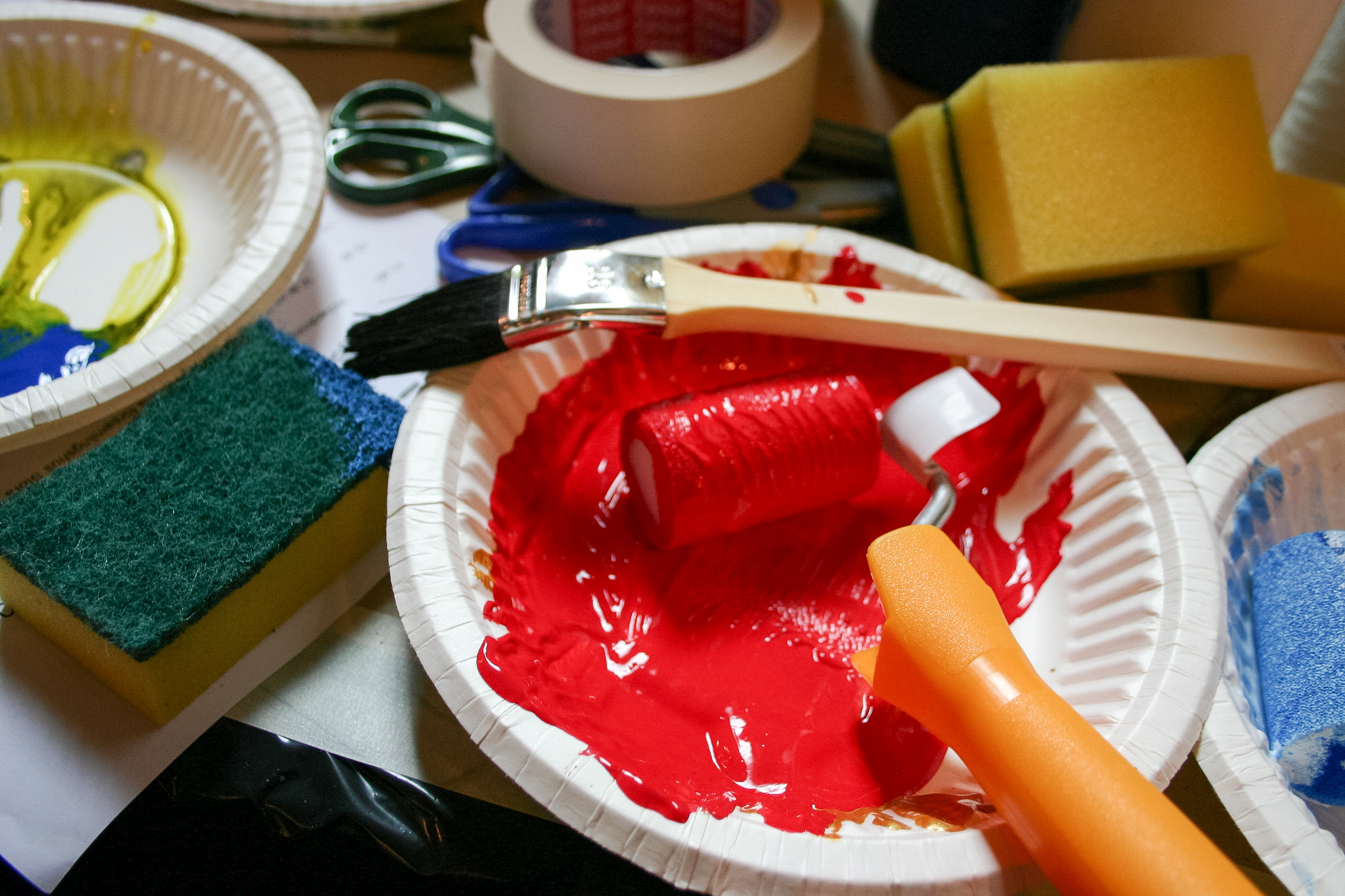 Papperstallrikar med målarfärg, penslar och tvättsvampar ligger på ett bord.