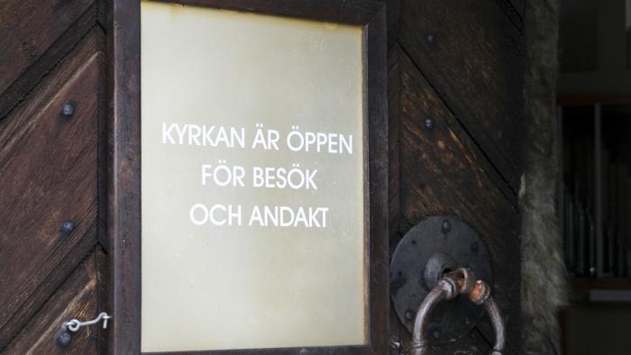En skylt med texten Kyrkan är öppen för besök och andakt hänger på en dörr.