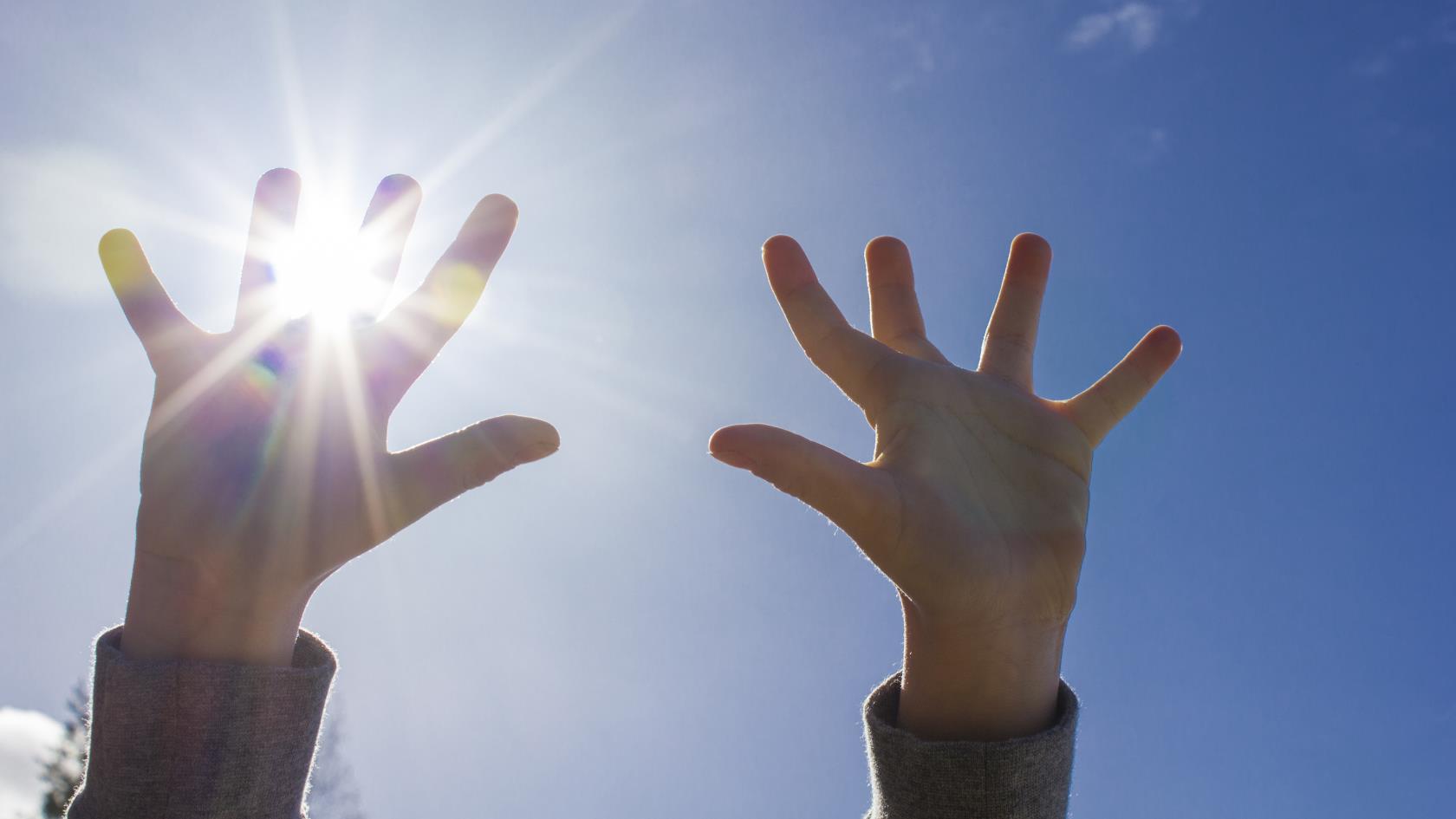 Ett barn sträcker upp händerna mot himlen. Solen lyser igenom fingrarna.