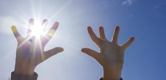 Ett barn sträcker upp händerna mot himlen. Solen lyser igenom fingrarna.