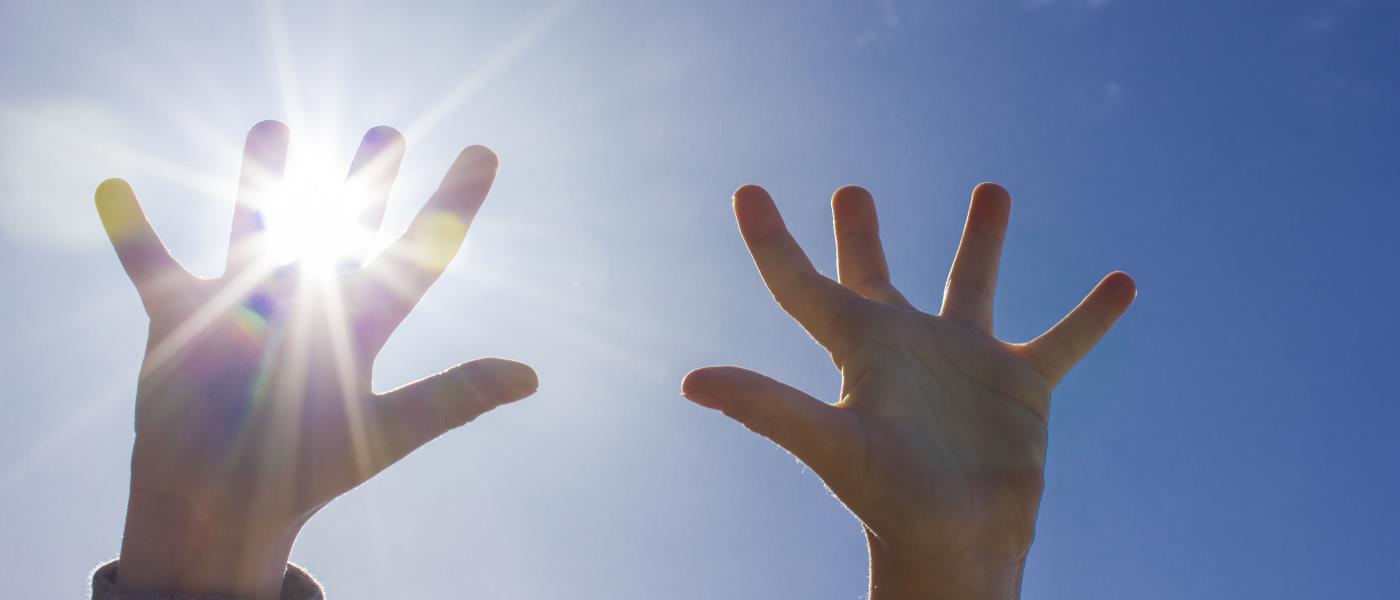 Ett barn sträcker upp händerna mot himlen. Solen lyser igenom fingrarna.