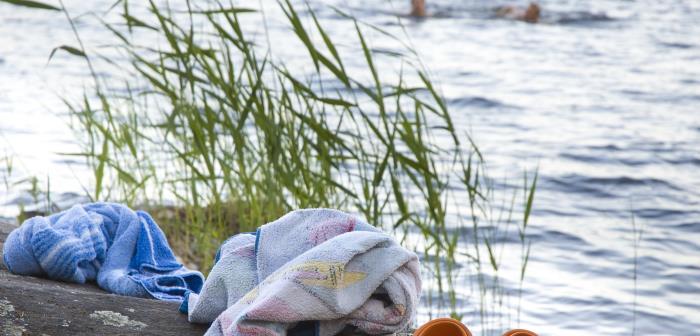 Ett par tofflor och två handdukar ligger på en klippa. Två personer badar i bakgrunden.