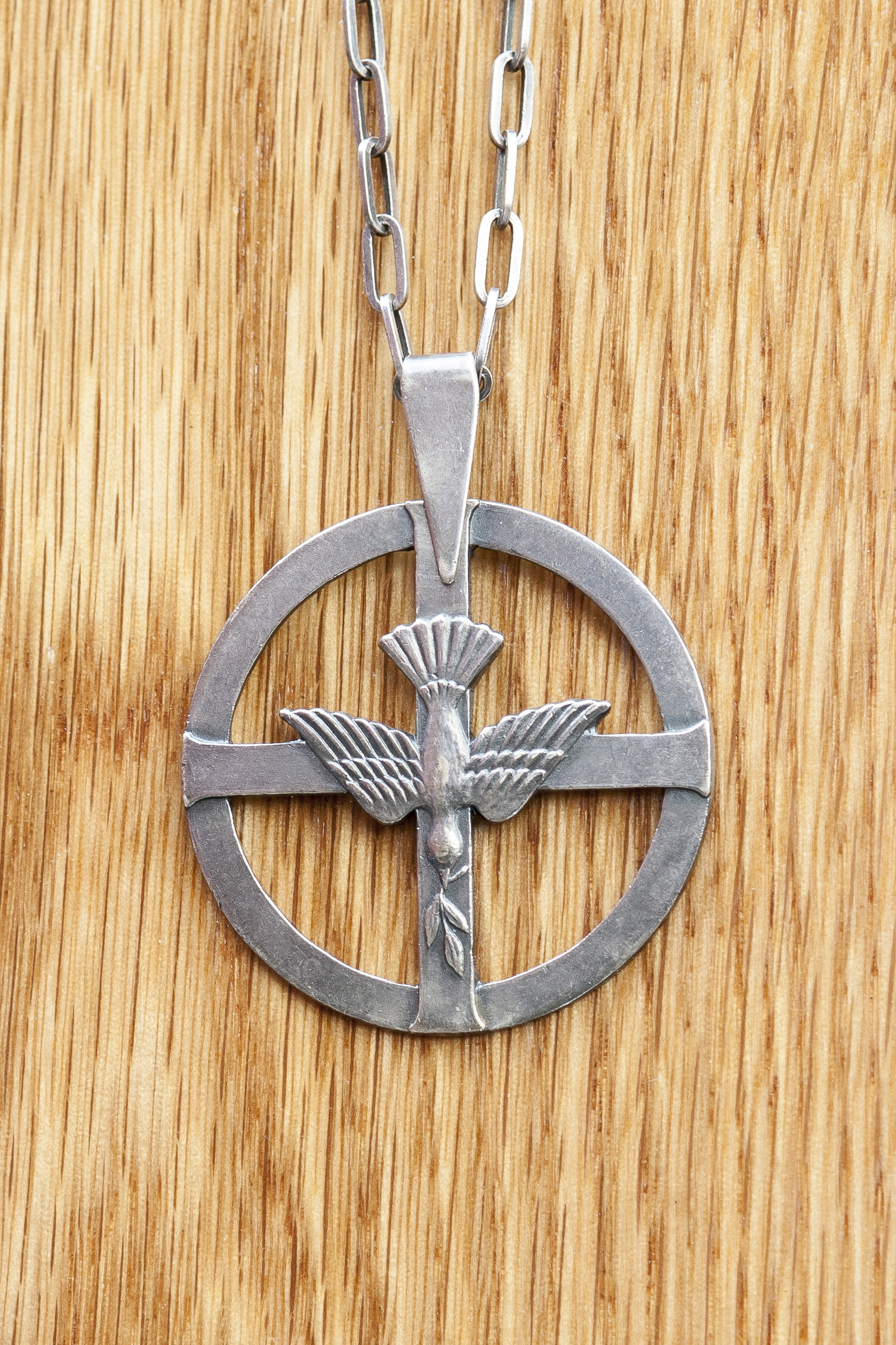 Diakonemblemet i silverfärg består av en cirkel och ett kors centrerat över cirkeln. Mitt i korset är en duva med en kvist i näbben.