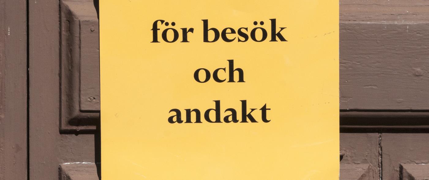En gul lapp med texten Kyrkan öppen för besök och andakt sitter på en dörr.