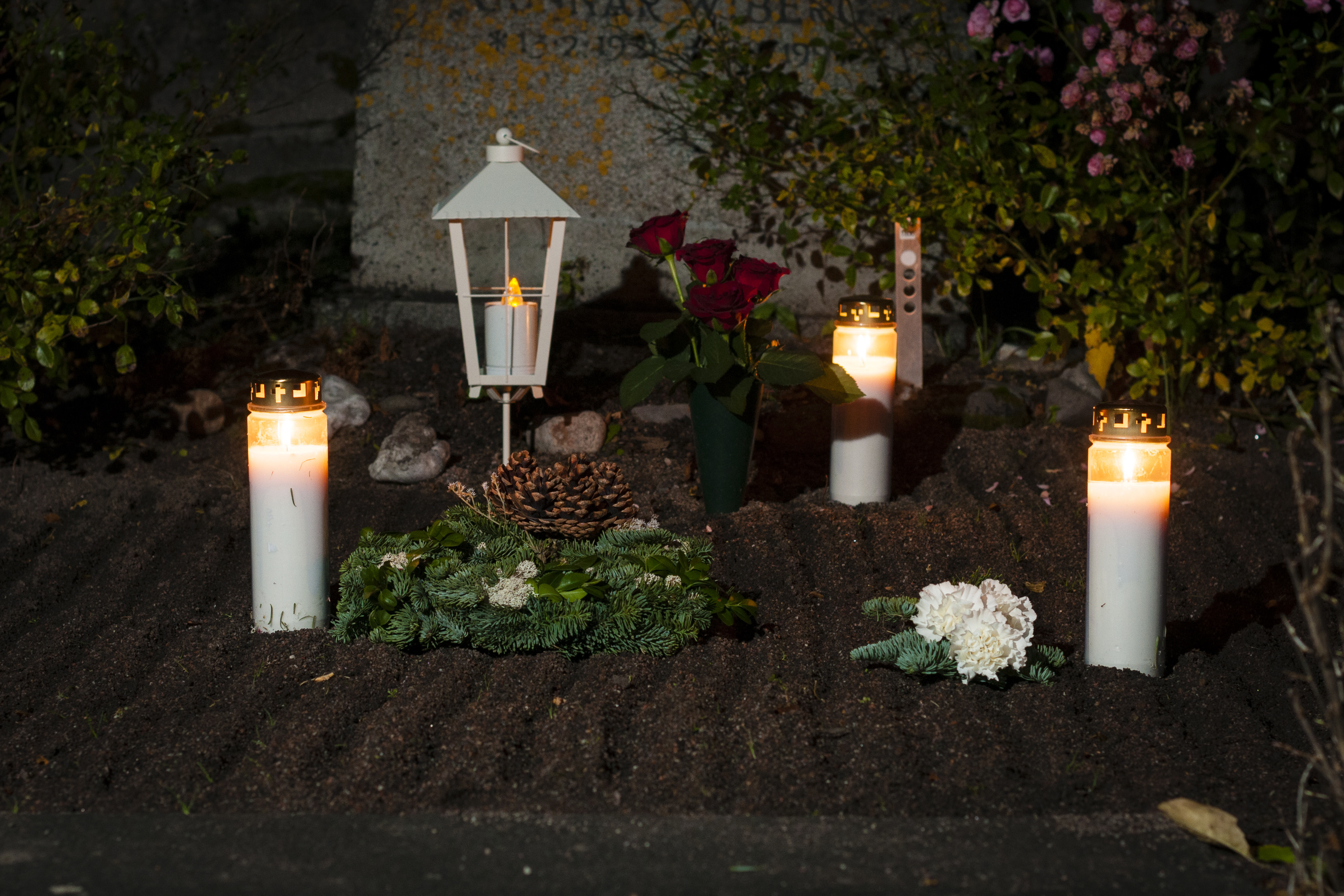 Tända ljus, kransar och rosor på en gravplats.