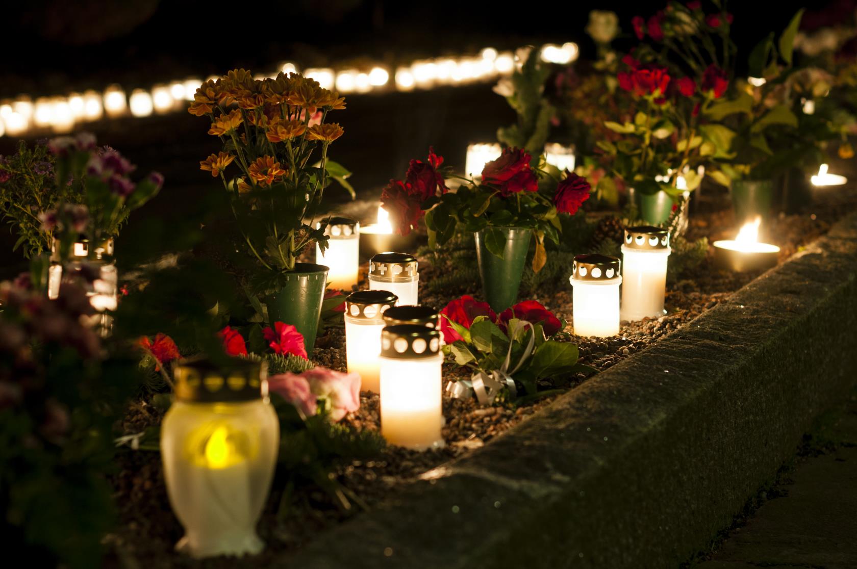 En massa blommor och tända gravljus lyser i mörkret på en minneslund.