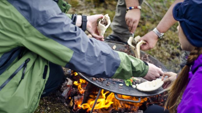 Några personer lagar mat över en eld utomhus.