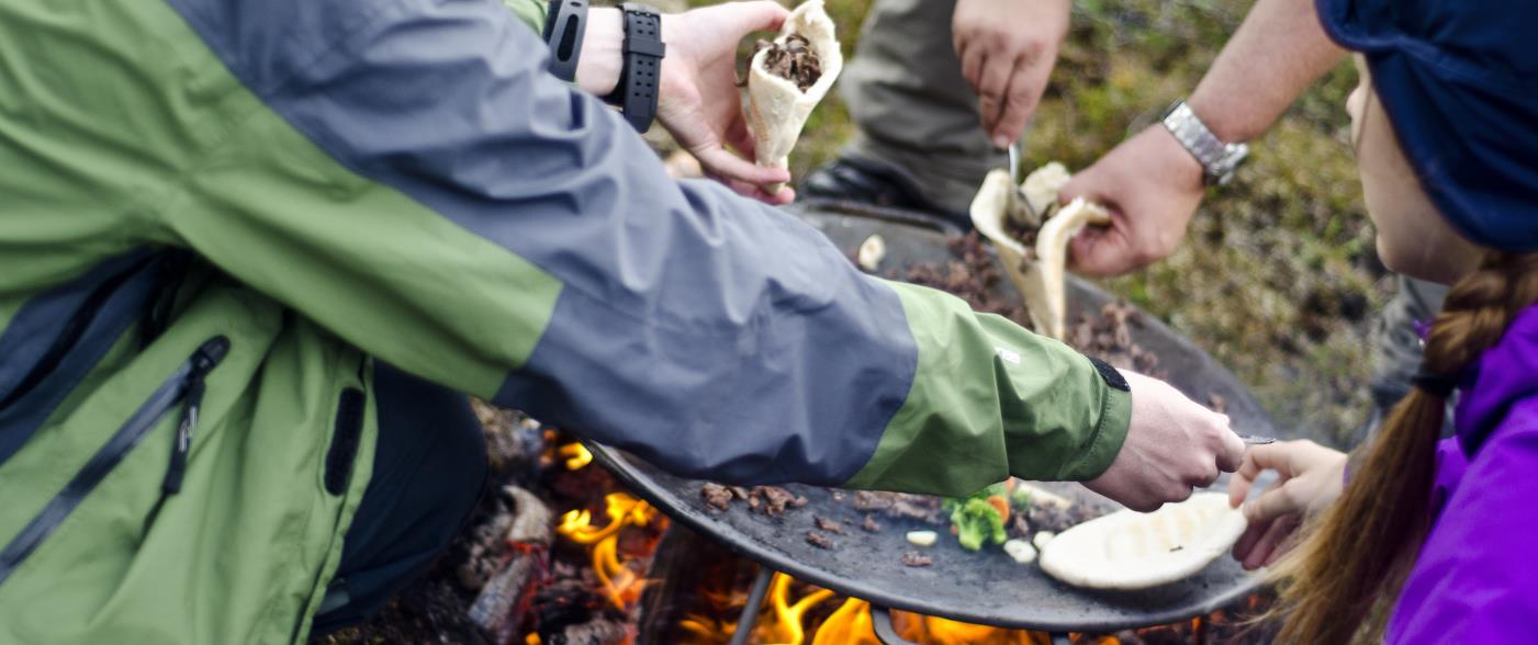 Några personer lagar mat över en eld utomhus.