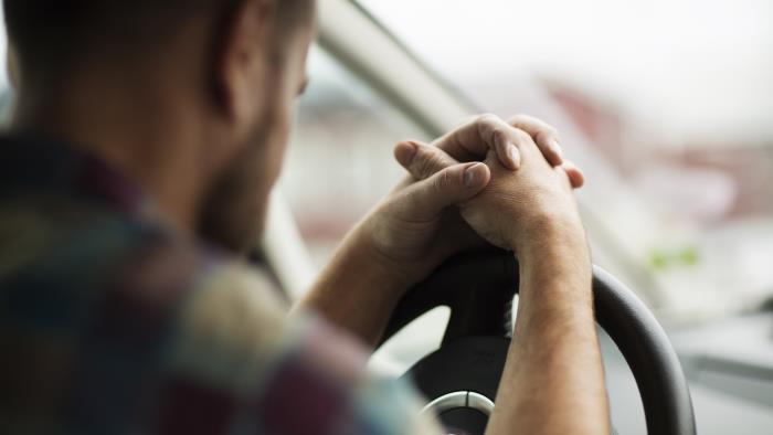 En man sitter i bilen med händerna knäppta på ratten.