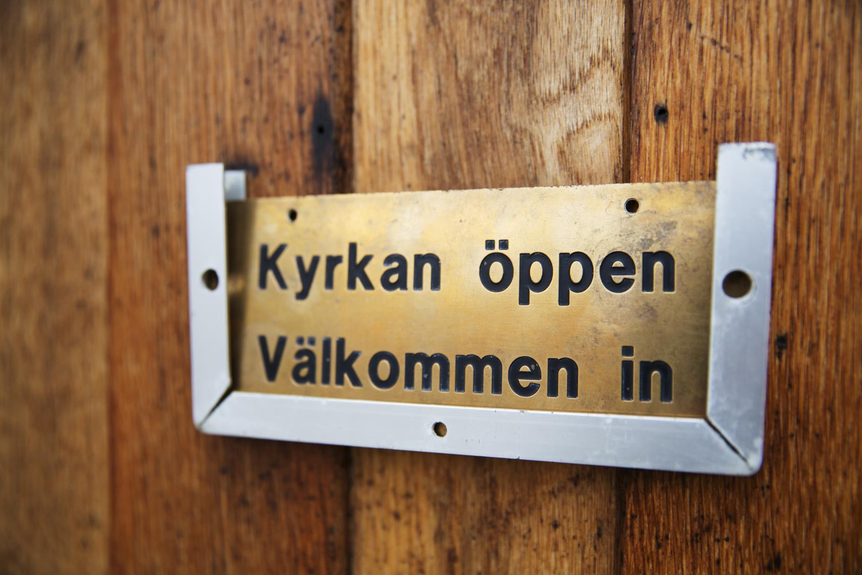 En skylt på en dörr med texten Kyrkan öppen välkommen in.