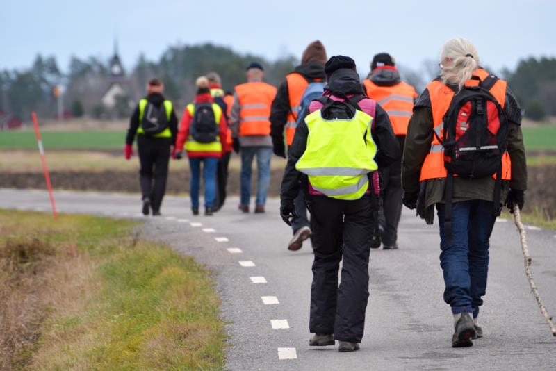 En grupp människor med reflexvästar går tillsammans på en landsväg.