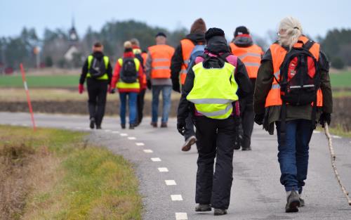 En grupp människor med reflexvästar går tillsammans på en landsväg.