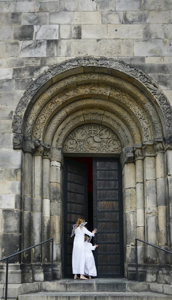 Två personer utklädda till änglar går in genom en kyrkport.