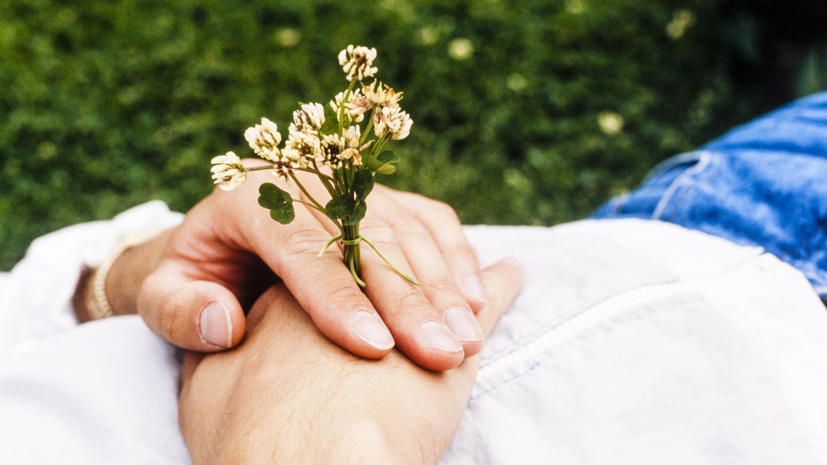 Någon ligger i gräset med en liten blombukett i handen.