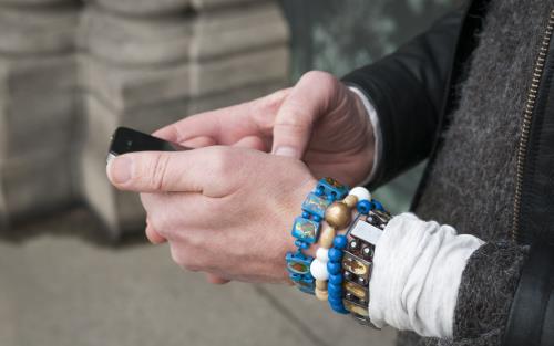 En person med flera armband håller på med sin mobiltelefon.