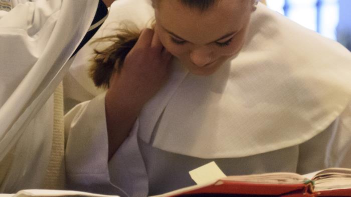 En ung tjej i vit konfirmationsdräkt blir döpt.