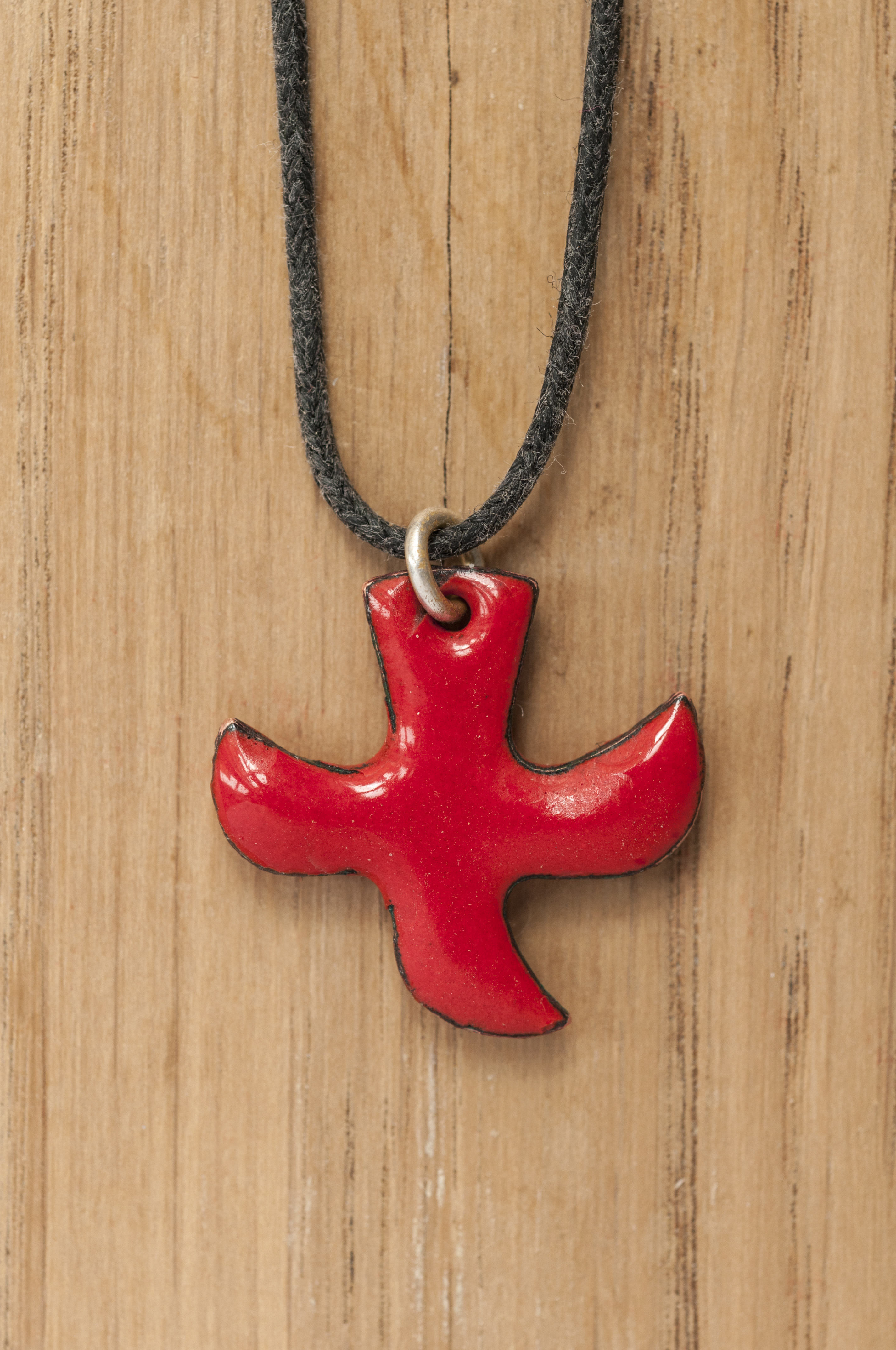 Närbild på ett halsband med ett rött Taizékors mot träbakgrund.
