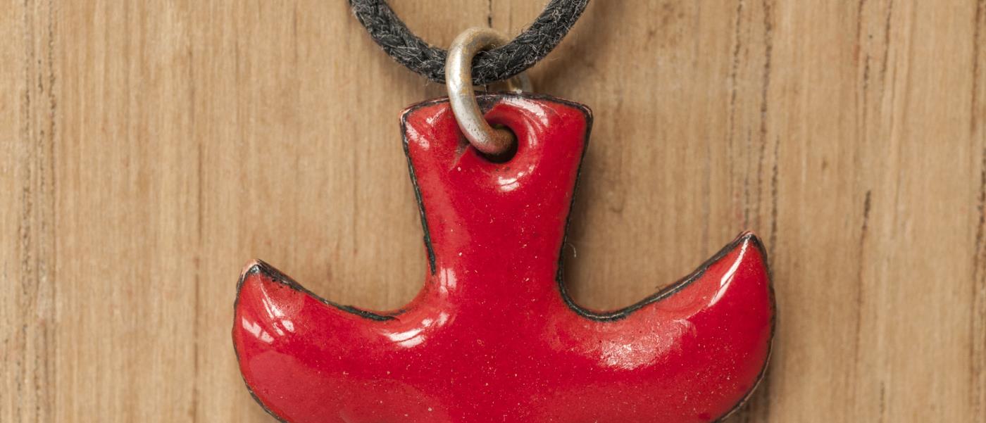 Närbild på ett halsband med ett rött Taizékors mot träbakgrund.