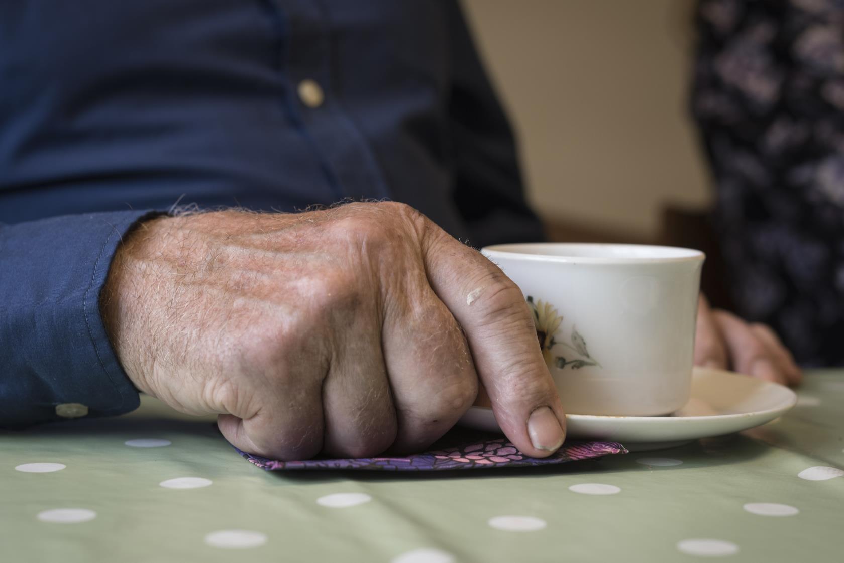 Närbild på en äldre mans hand som håller i en kaffekopp.