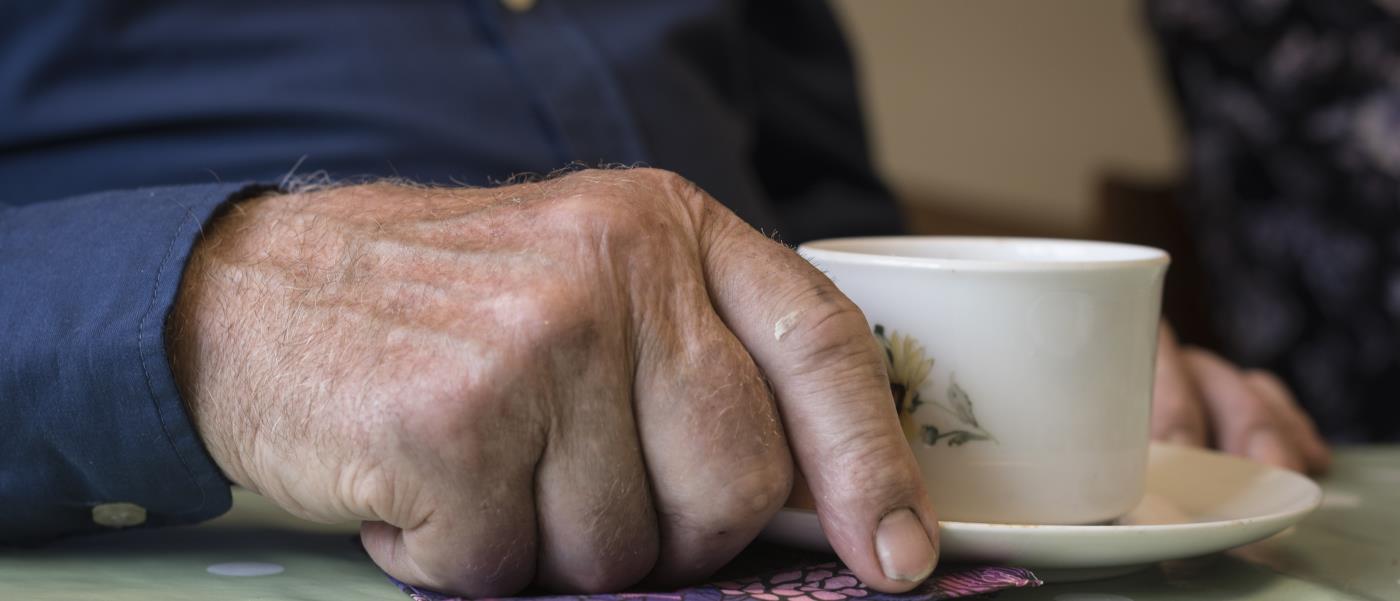 Närbild på en äldre mans hand som håller i en kaffekopp.