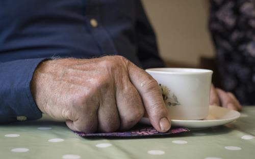 Närbild på en äldre mans hand som håller i en kaffekopp.