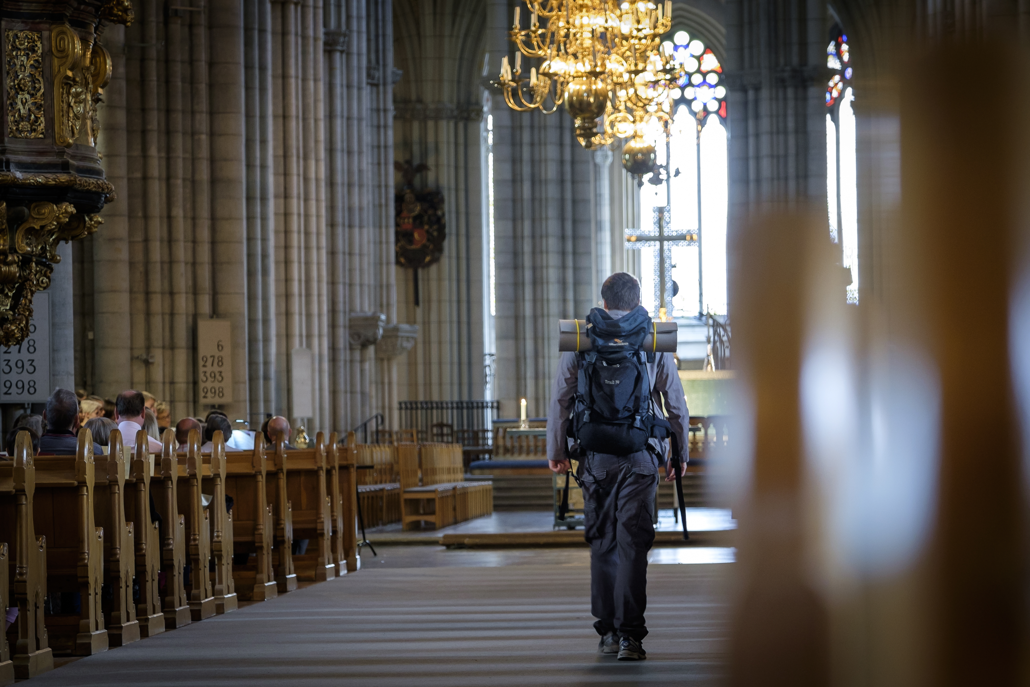 En man med stor ryggsäck går mellan kyrkbänkarna i Uppsala domkyrka.