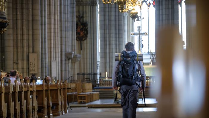 En man med stor ryggsäck går mellan kyrkbänkarna i Uppsala domkyrka.