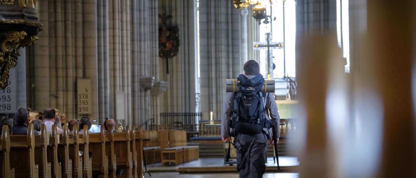 En man med stor ryggsäck går mellan kyrkbänkarna i Uppsala domkyrka.