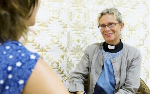 En kvinnlig präst samtalar med en kvinna inomhus.