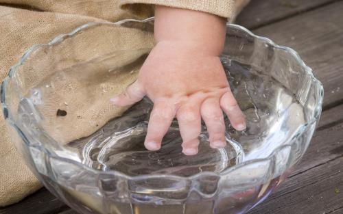 En bebis doppar handen i en skål med vatten.