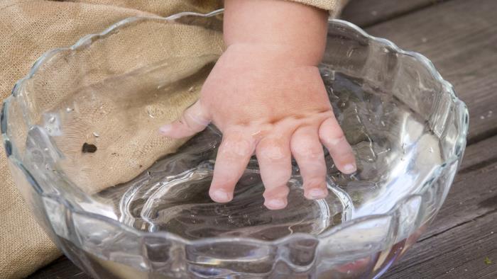 En bebis doppar handen i en skål med vatten.