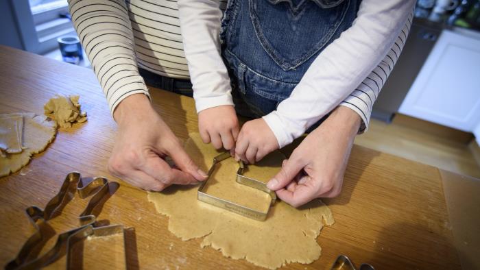 En vuxen hjälper ett barn trycka ner en form i pepparkaksdegen på bordet.