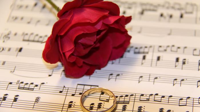 En röd ros och en guldfärgad ring ligger på ett notblad.