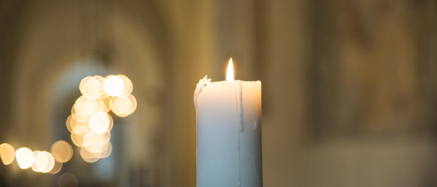 Ett tänt stearinljus i en kyrka.