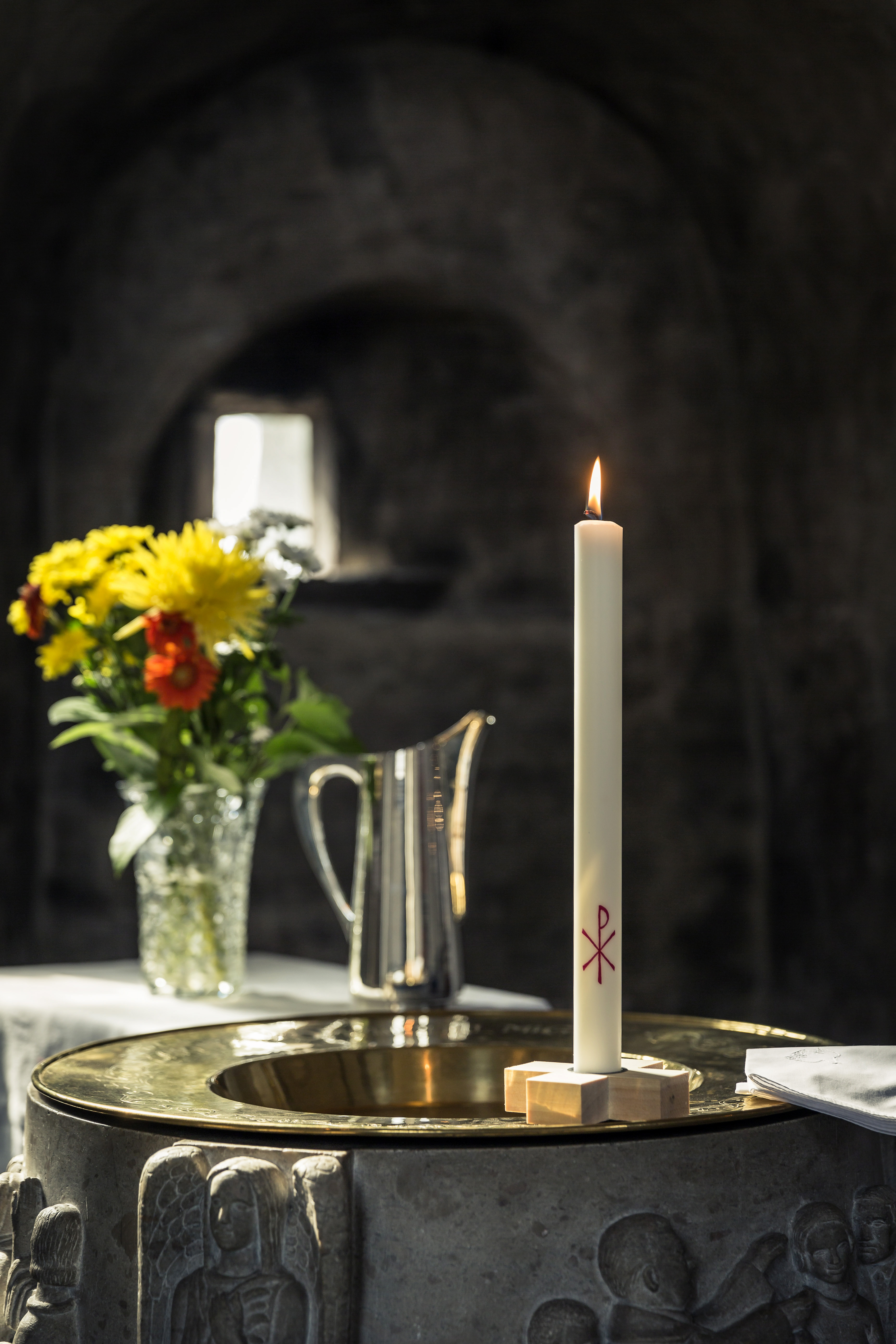 Ett tänt ljus står på en dopfunt.