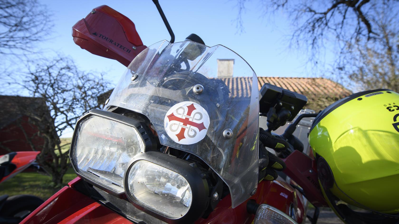 Ett klistermärke med ett pilgrimskors sitter på rutan på en motorcykel.