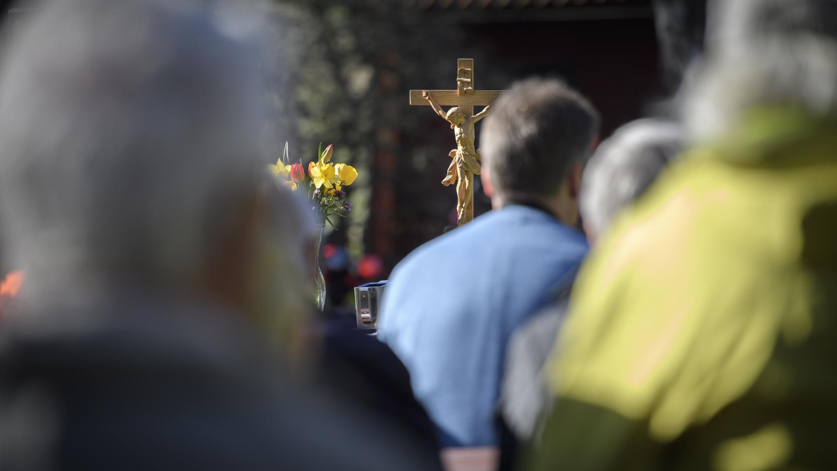 Ett altare med ett träkrucifix. Suddiga människor i bakgrunden.