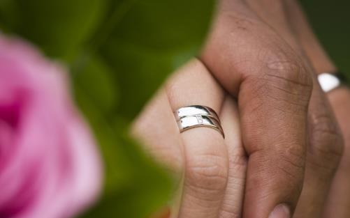 Närbild på två personer med vigselringar som håller hand.