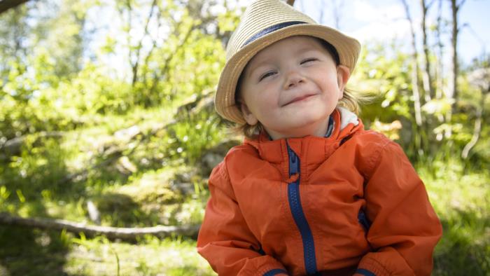 En liten pojke med halmhatt sitter ute i naturen och ler mot kameran.