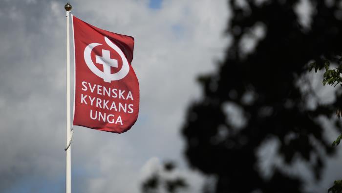 En flaggstång med en röd flagga med texten Svenska kyrkans unga och deras symbol.