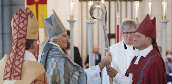 Ärkebiskop Antje Jackelén räcker över en biskopsstav till en biskop i röd kåpa.