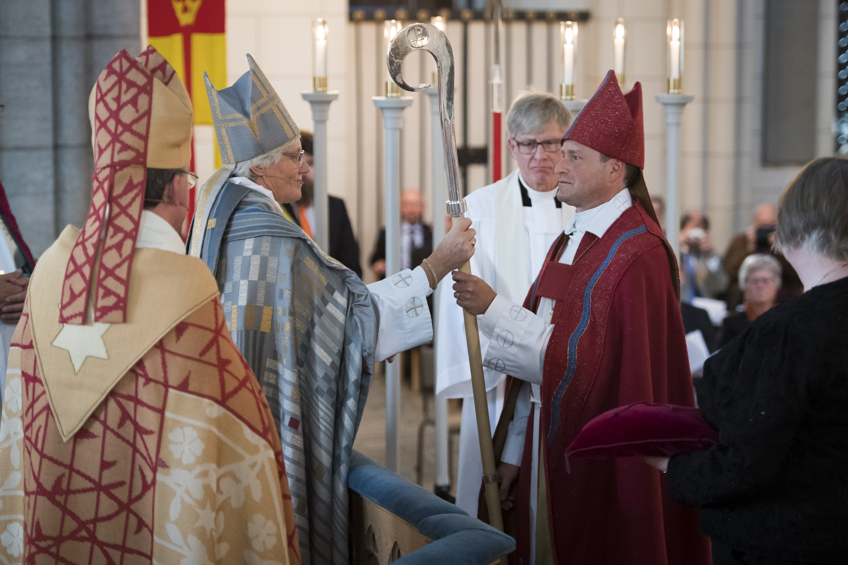 Ärkebiskop Antje Jackelén räcker över en biskopsstav till en biskop i röd kåpa.